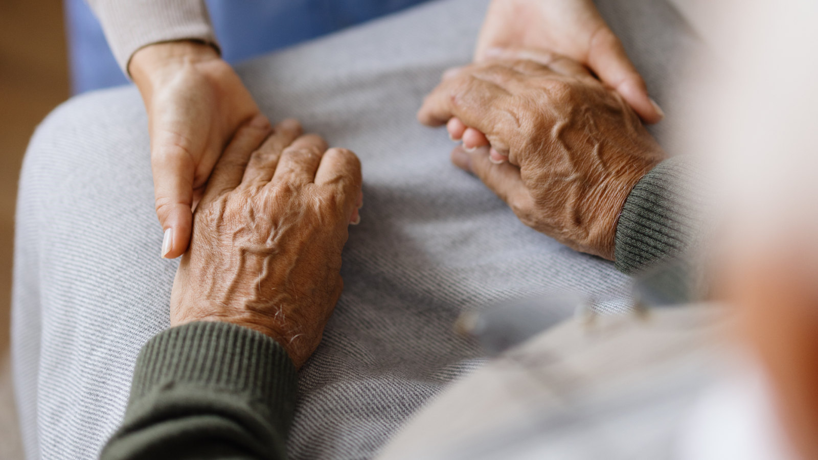 Hand einer Pflegekraft, die die Hände einer älteren Person hält